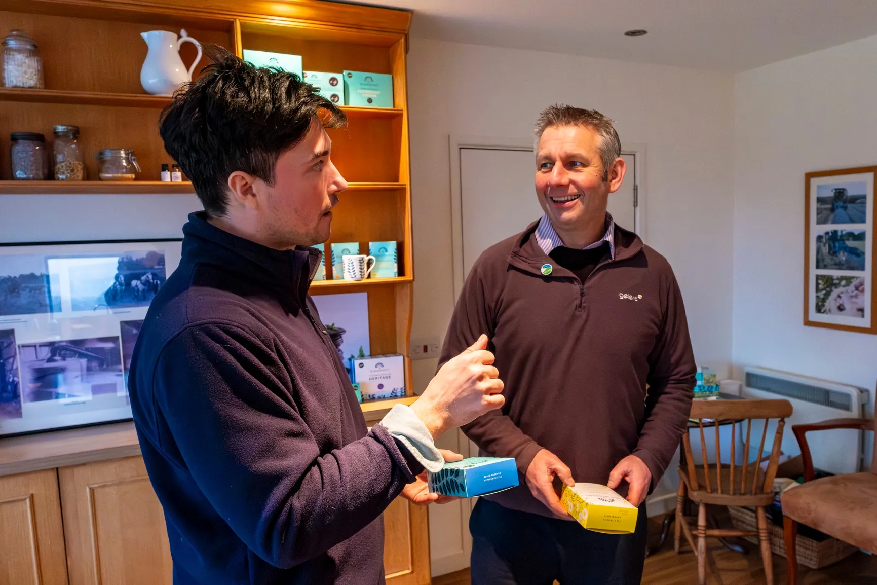 Two people in conversation smiling, holding boxes of tea in a tea shop.