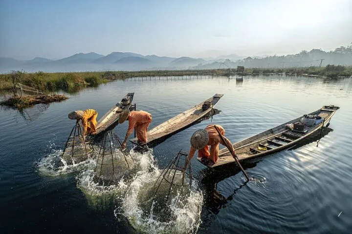 Fischer mit traditionellen Netzen und Holzbooten auf einem See.