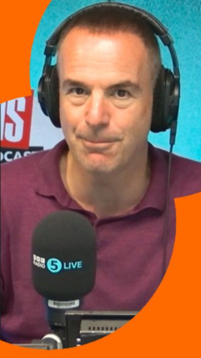Martin Lewis has short dark hair and is wearing radio headphones and a purple polo-shirt. He is sat in front of a radio microphone.