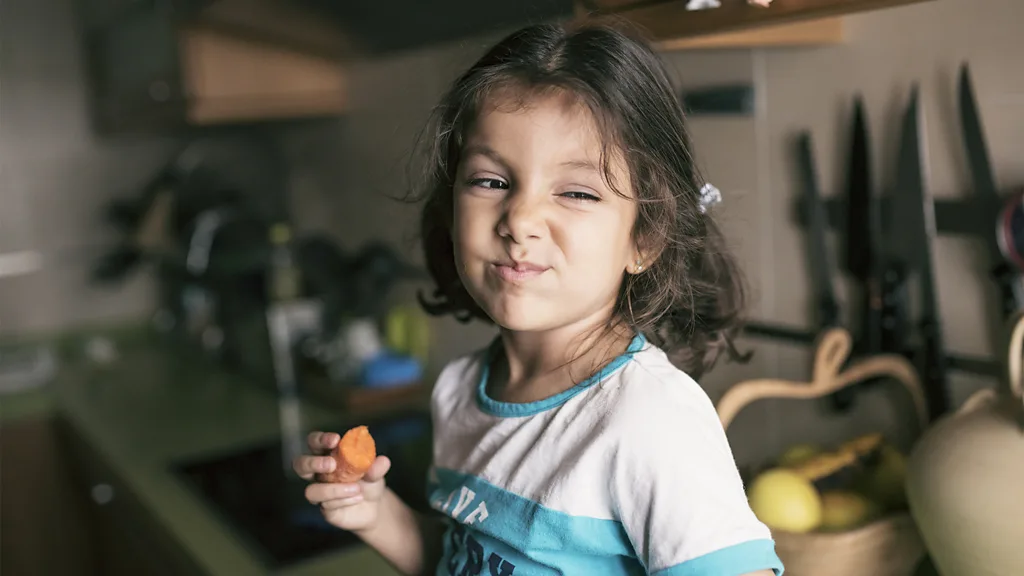 A young girl chewing and holding a carrot
