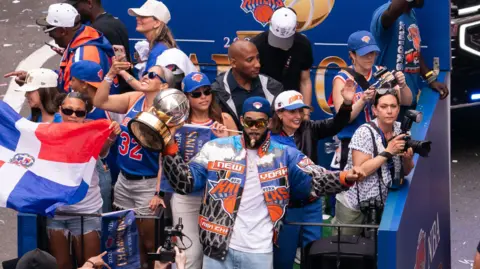 A group of people celebrating on a float - one man holding a big gold trophy 