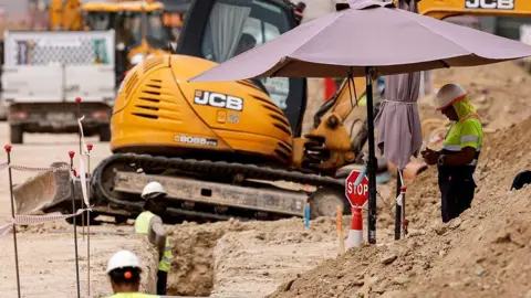 Getty Images A worker shelters under an umbrella on a building site in Madrid