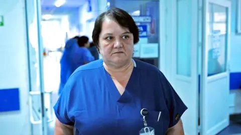 Surgeon Dr Oana Goidescu on shift at Buzu0103u Hospital in blue scrubs. She has mid length black hair