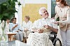 Smiling elder man on wheelchair with braided blanket on legs and reads book