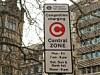 London Congestion Charging Central Zone road sign with hours listed, seen through tree branches.