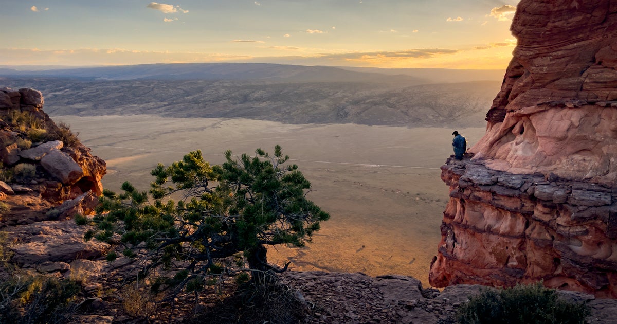 Milagra, Condor 1221, perches on a rocky cliffside overlooking a valley during sunset. 
