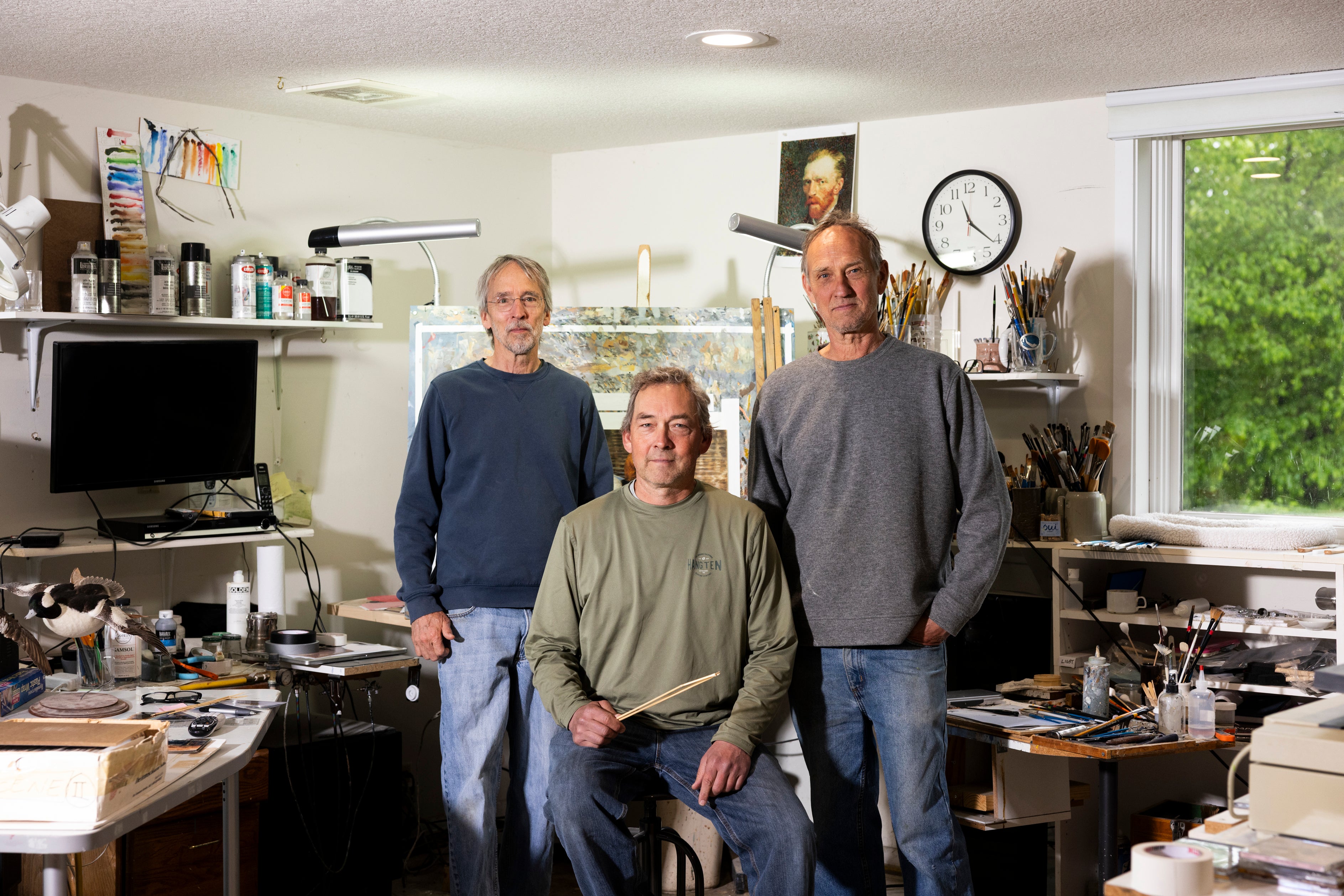 The three brothers pose for a portrait in Jim's home studio filled with paints and brushes, and a picture of Vincent Van Gogh on the wall.
