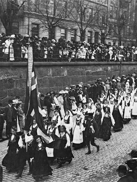 Black and white photo of young people in a parade, wearing national costumes, holding