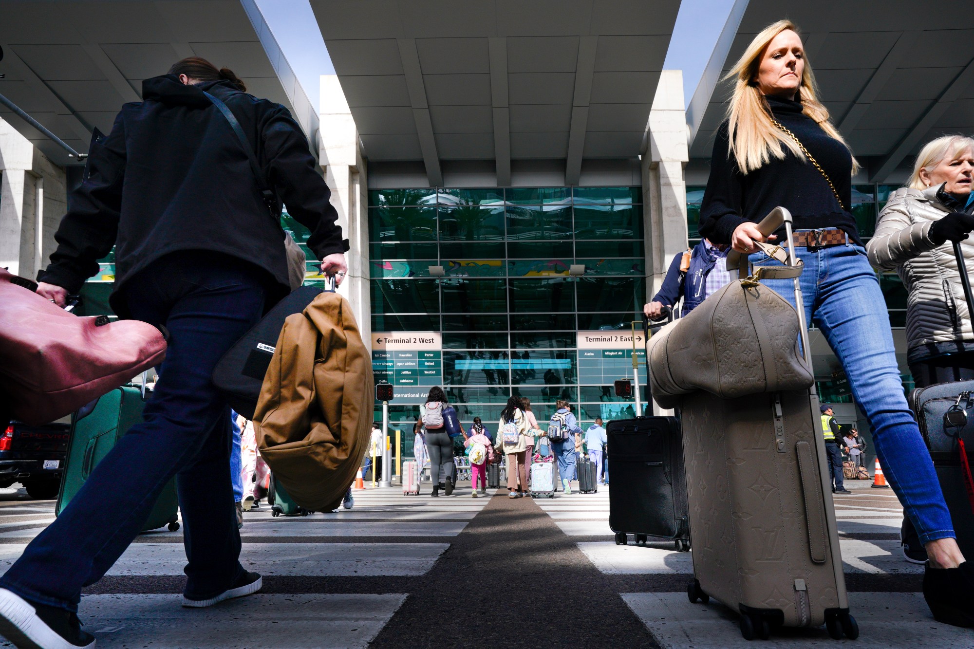 At San Diego International Airport on Tuesday, Nov. 26, 2024, airline passengers arriving and departing enter the crosswalk with their luggage in tow.  (Nelvin C. Cepeda / The San Diego Union-Tribune)
