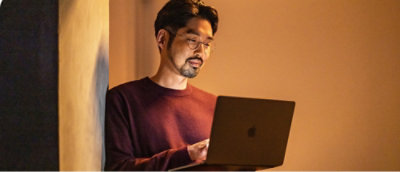 A man in a maroon shirt and glasses using a laptop.