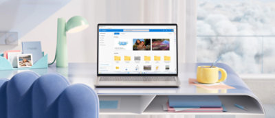 A laptop displaying a file management app is on a desk with a blue chair, yellow mug, teal lamp