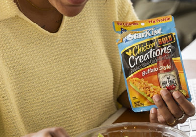 A person in yellow holds StarKist Chicken Creations Buffalo Style over a salad; pack shows 90 calories and 11g of protein.