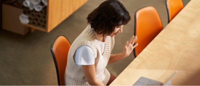 Seorang perempuan mengenakan sweter putih sedang duduk di dekat meja.