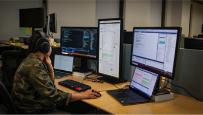 Kaitseriietuses naine istub laua taga, millel on kaks monitori.