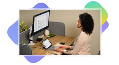 אדם יושב ליד שולחן עבודה, מרכיב אוזניות ועובד על מכשיר Tablet המחובר לצג של מחשב שולחני.