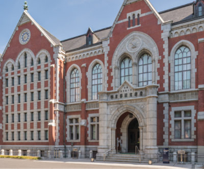 A historic red brick building with arched windows and a central entrance, featuring intricate stone details