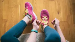 Gros plan sur une femme en leggings verts qui lace ses chaussures de sport roses et jaunes. On voit ses avant-bras et elle porte une montre verte.