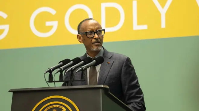 Perezida w'u Rwanda Paul Kagame arimo kuvuga ijambo avugira mu ndangururamajwi enye ziri ku meza maremare yo kuvugiraho ijambo, ariho ikirango cya Repubulika y'u Rwanda. Yambaye indorerwamo, ikositimu yijimye ijya kuba ubururu, karuvati y'ikigina, n'ishati ijya kuba ubururu bwerurutse. Arareba ahagana ku ruhande. Inyuma he hari ikirango cy'icyatsi kibisi n'umuhondo, cyanditseho mu mweru mu cyapa ngo 'GODLY', andi magambo ntaboneka ku ifoto. Ifoto yo ku cyumweru, i Kigali, ku itariki ya mbere Gashyantare (2) mu mwaka wa 2026. 