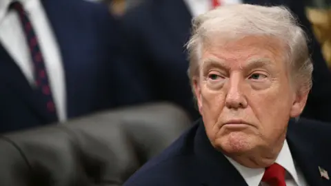 Donald Trump looks to the left of frame while wearing a suit and red tie in the White House Oval Office on Thursday.