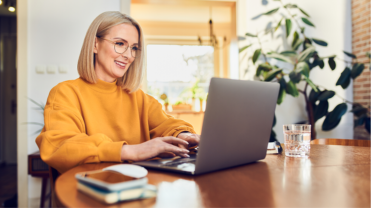 A woman working from home. She’s on her laptop at the dining room table.