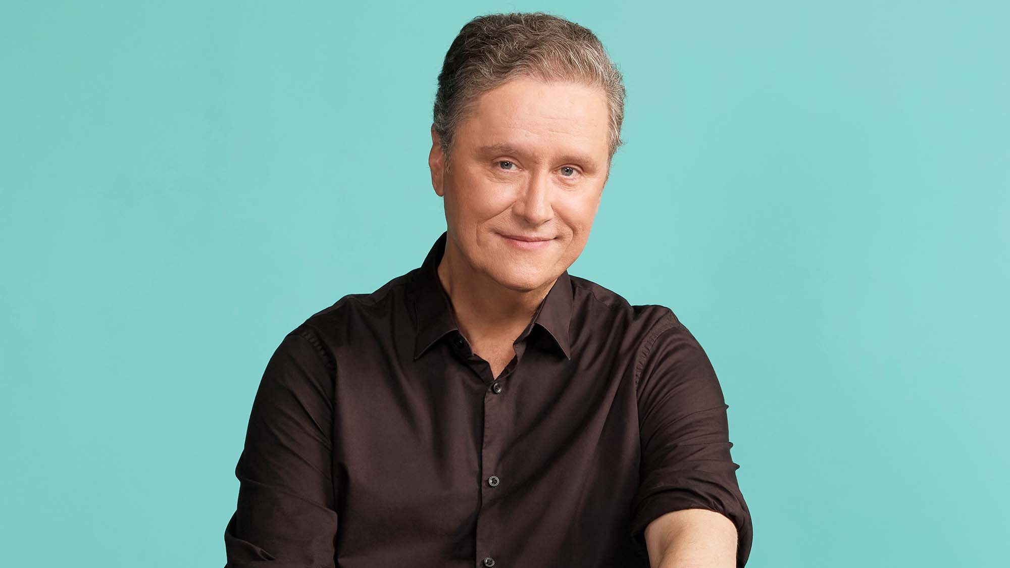 A man sitting on a stool with hands on thighs looking at the camera