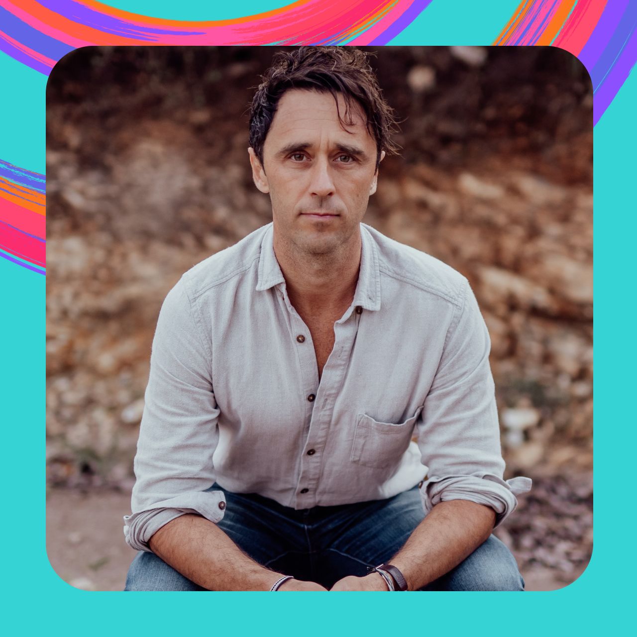 Aaron Tait sits in front of a natural scene outside.