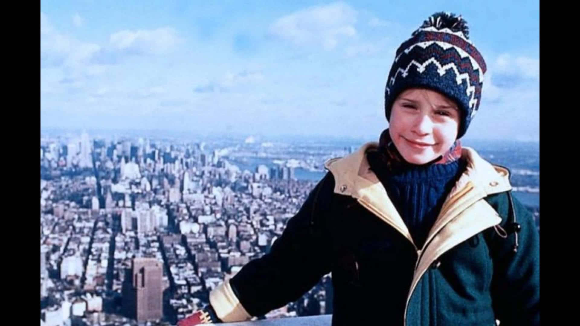A Boy In A Hat And Jacket Standing On Top Of A Building