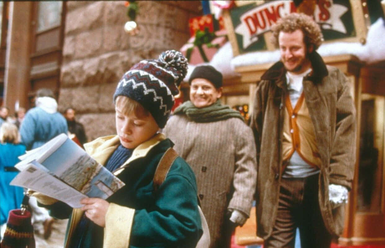 A Boy Is Reading A Newspaper In Front Of A Man And Woman
